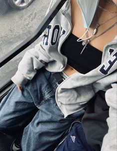 a woman wearing jeans and a hoodie is sitting in the back of a car