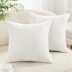 three white pillows sitting on top of a couch next to a cup and saucer