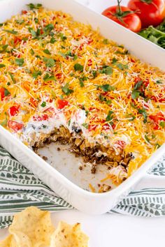 a casserole dish with cheese, tomatoes and other toppings in it next to some tortilla chips