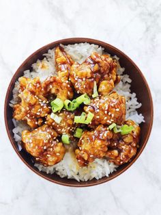 a bowl filled with chicken and rice covered in sesame seeds on top of a marble table