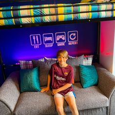 a young boy sitting on top of a couch under a bunk bed with colorful pillows