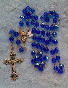 "Offering you a handmade new crystal bead rosary made in the Czech Republic. The 8mm beads are medium sapphire blue crystal with an aurora borealis (AB) finish. Entire rosary is 18K gold plated. Italian made & designed crucifix measures 2\" long x 1-1/4\" wide. Rosary length is 23\" long. Comes gift boxed with card of origin." Blue Rosary With 8mm Beads And Crucifix, Blue Rosary With 8mm Beads In Cross Shape, Blue Rosary With Round Beads For Healing, Blue Rosary With 8mm Beads For Healing, Spiritual Blue Rosary With Round Beads, Blue Rosary For Healing, Blue Healing Rosary, Blue Rosary, Dark Garnet