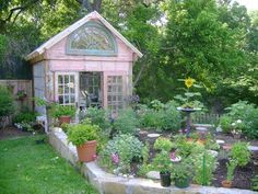 a garden shed with potted plants and flowers in the foreground, surrounded by trees