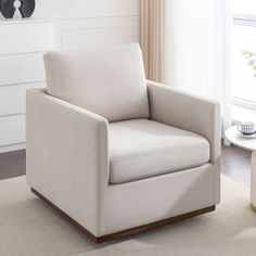 a white chair sitting on top of a rug in a living room next to a window