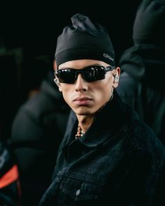 a young man wearing sunglasses and a black hat is looking at the camera while standing in front of other people