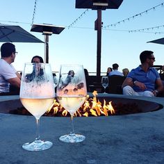 two wine glasses sitting next to each other on top of a fire pit in front of people