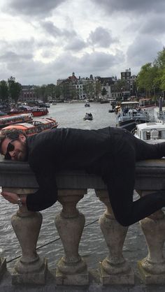 a man laying on top of a stone fence next to water