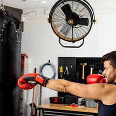 a man wearing red boxing gloves in a gym with a fan hanging from the ceiling