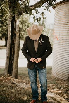 a man wearing a cowboy hat standing in front of a tree with his hands on his hips