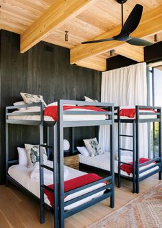 three bunk beds with red and white pillows in a room that has wood paneling on the ceiling