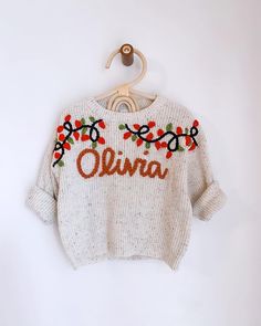 a white sweater with red flowers and the word ohana on it hanging from a wooden hanger