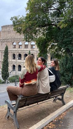 three women sitting on a bench in front of the colossion