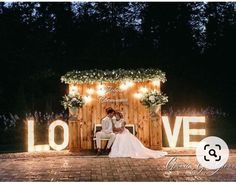 a bride and groom sitting on a bench in front of a love sign at night