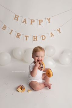 a baby sitting on the floor eating a doughnut with happy birthday banner in background