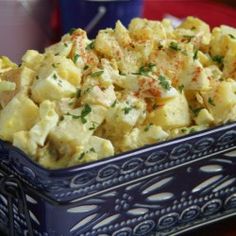 a blue bowl filled with potato salad on top of a red tablecloth next to a cup