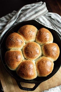 a skillet filled with bread rolls on top of a wooden cutting board next to a towel