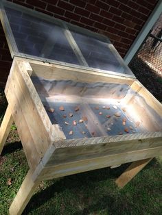 a wooden box with glass inside sitting in the grass next to a brick wall and fence