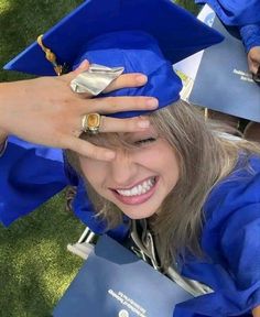 a woman wearing a blue graduation cap and gown holding her hands to her head while smiling at the camera