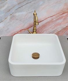 a white square sink with a faucet on the side and a gold faucet