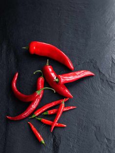 several red peppers on a black surface with one pepper still attached to the end of the chili