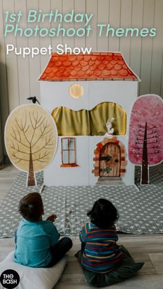 two children sitting on the floor in front of a paper house