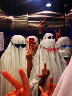 several people in white heads covering their faces and making the peace sign with their fingers