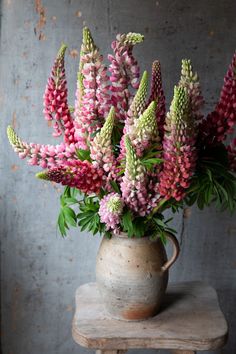 a vase filled with pink and green flowers sitting on top of a wooden table next to a gray wall