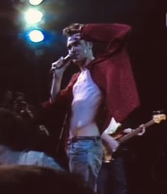 a man standing in front of a microphone on stage with his shirt over his head