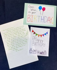 two birthday cards are sitting next to each other on a black surface, one has an open notepad and the other has a happy birthday message