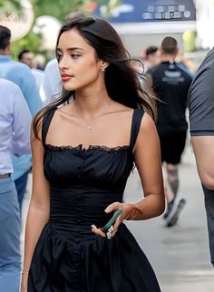 a woman in a black dress is walking down the street with her hand on her hip