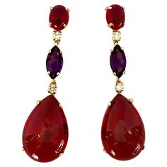 Red and purple colors glow in these statement dangle earrings. Brightly colored cabochon rhodolite garnet (origin: Tanzania) is complimented by richly colored marquise cut amethyst (origin: Brazil). The gems support cabochon red topaz (origin: Brazil) which are expertly cut and polished into pear shapes. White diamonds add extra sparkle. The mountings are fabricated in 18k yellow gold. The one-of-a-kind earrings come with posts and jumbo friction baks. Pear Shapes, Red Topaz, Diamond Red, Red And Purple, Rhodolite Garnet, Marquise Cut, Tanzania, Pear Shaped, Diamond White