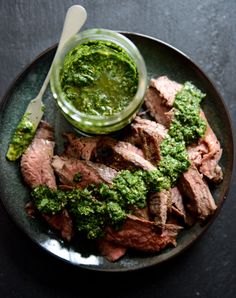 a plate with meat, broccoli and pesto on it next to a jar of sauce