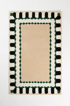 an area rug with black, white and green designs on the border in front of a wall