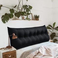 a bed with a black headboard next to a potted plant