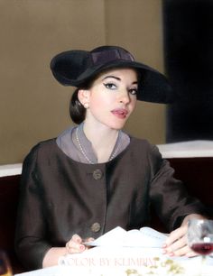 a woman sitting at a table wearing a black hat