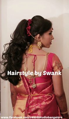 a woman with long black hair wearing a red and gold saree, standing in front of a white wall