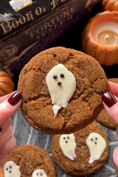 a person holding up a cookie with white icing on it and ghost faces in the middle