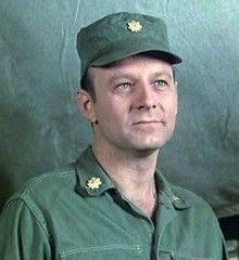 a man in green uniform standing next to a metal wall and looking at the camera