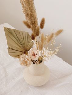 a white vase with dried flowers and an umbrella on top of a tableclothed surface