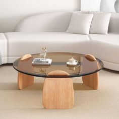 a glass coffee table with wooden legs in front of a white couch and pillows on the floor