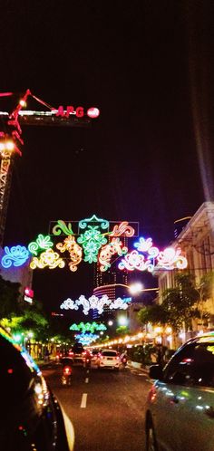 cars driving down the street at night with christmas lights in the sky and decorations on the buildings