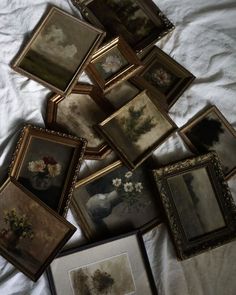 there are many framed pictures on the bed with white linens and one has flowers in a vase