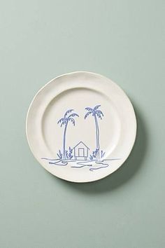 a white plate with blue palm trees and a small house on the front, against a pale green background