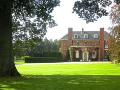 a large brick building sitting in the middle of a lush green field next to a tree