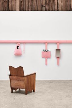 a wooden chair sitting in front of a white wall with pink hooks on it's sides