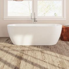 a white bath tub sitting on top of a wooden floor next to two large windows