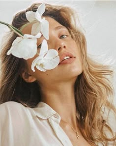 a woman with flowers in her hair looking up at the sky while she is wearing a white shirt