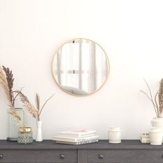 a table topped with vases and plants next to a round mirror on the wall