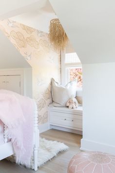 a white bed sitting under a window next to a pink rug on top of a hard wood floor