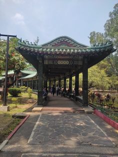 people are walking under a covered walkway in a park with lots of trees and plants